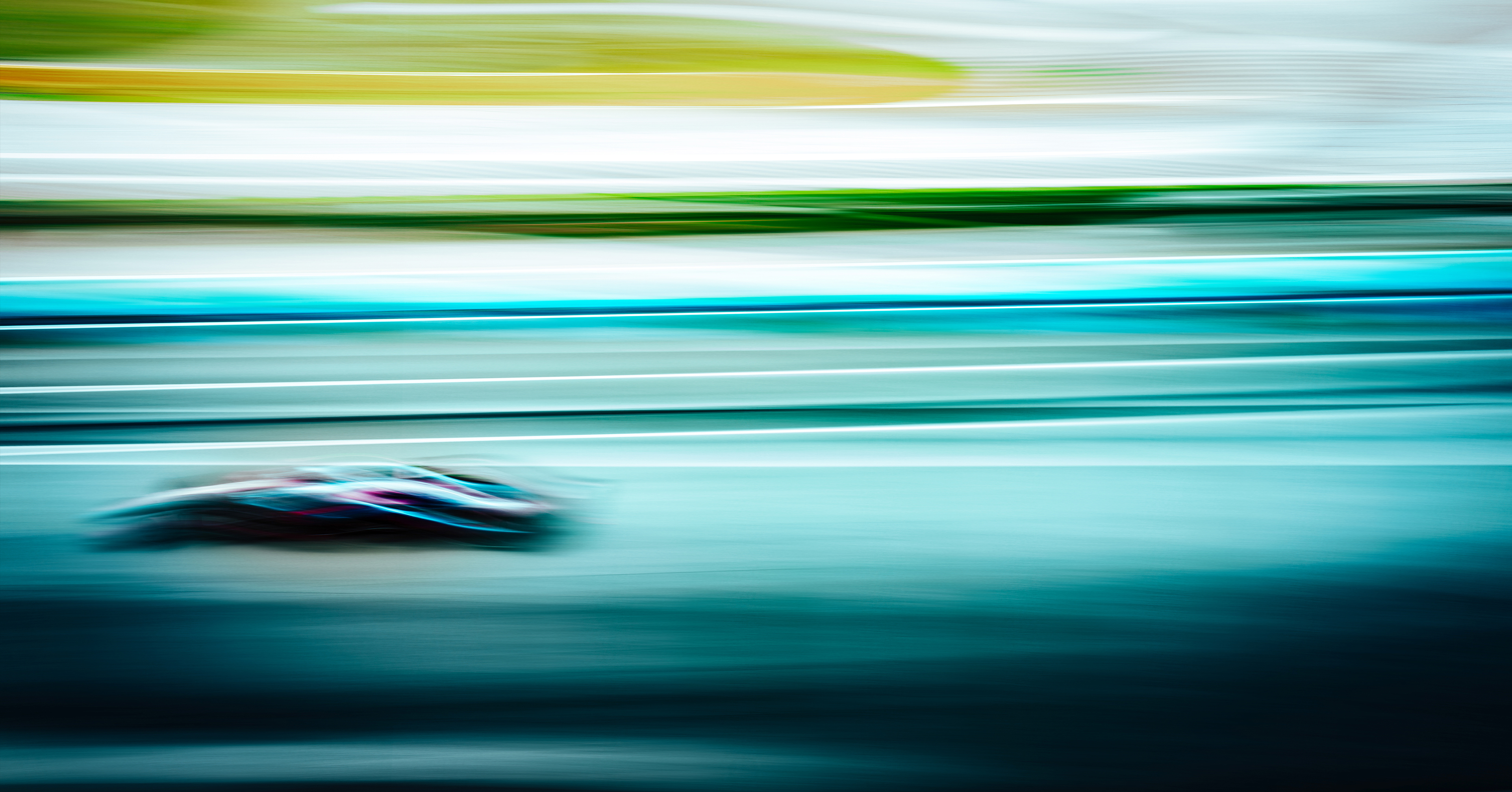 Dynamische Motorsportaufnahme mit verschwommenem Formel-Rennwagen und farbigen Bewegungsstreifen in Blau, Grün und Türkis.