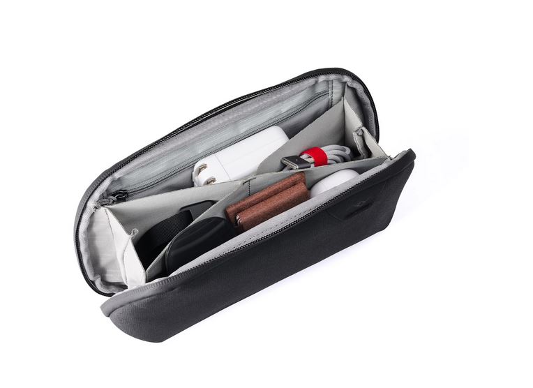 Blick in das weit geöffnete, hellgraue Innenfach einer schwarzen Peak Design Tech Pouch (Zubehörtasche), die schräg auf einer weißen Oberfläche steht. Die Grafik demonstriert das durchdachte Origami-Organisationssystem im Inneren, in dem verschiedene Allt